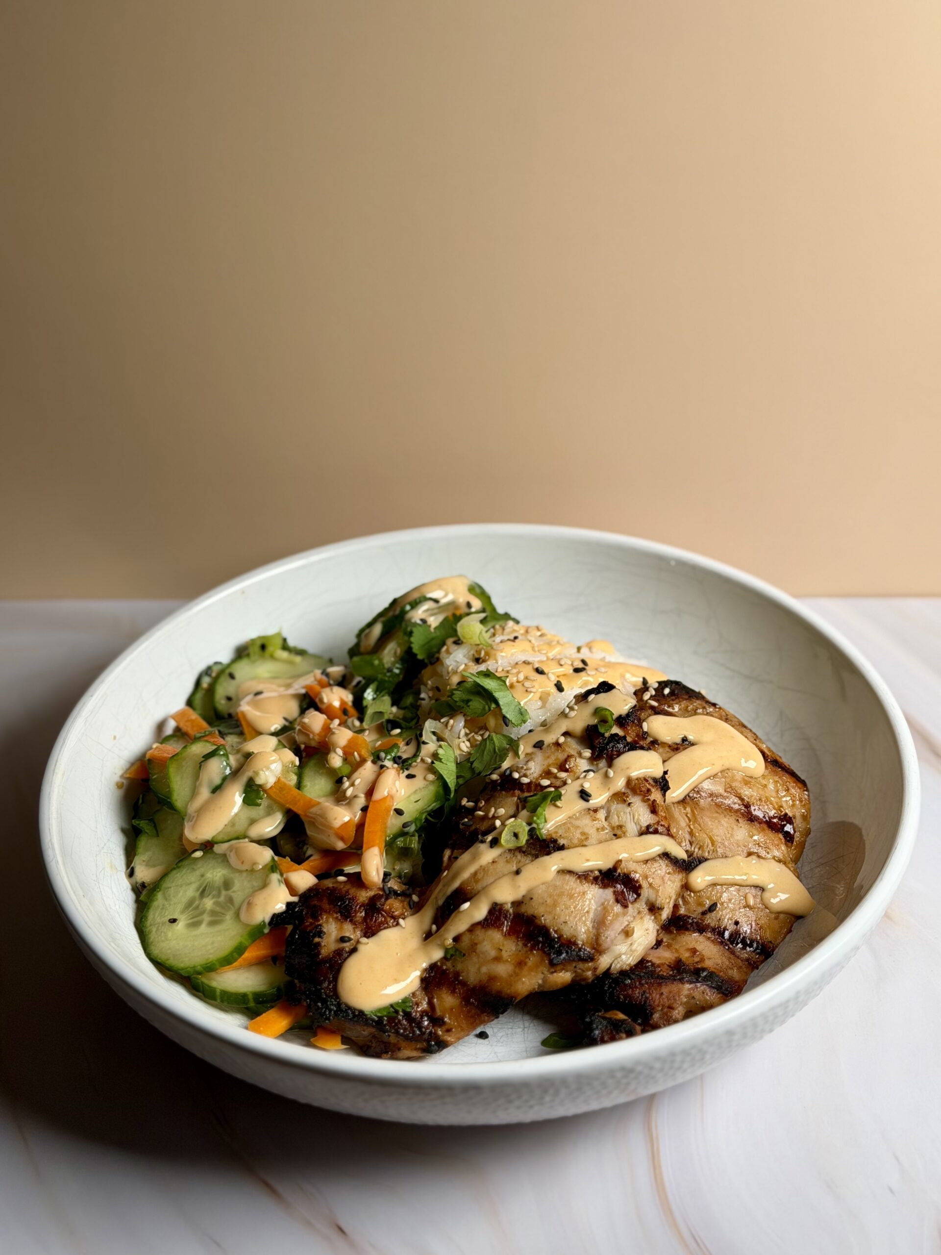 Asian-style chicken rice bowls with cucumber salad, rice, and creamy sriracha sauce