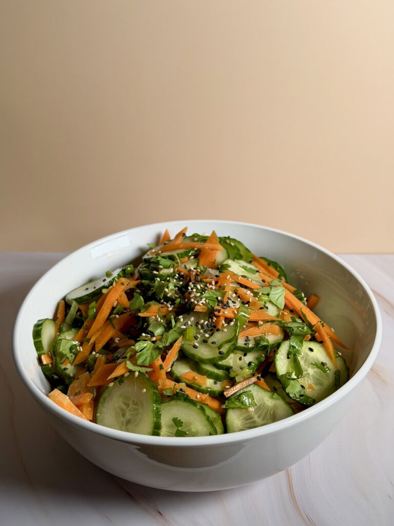 Asian-style cucumber salad with carrots, green onions, cilantro, and sesame seeds in a white bowl