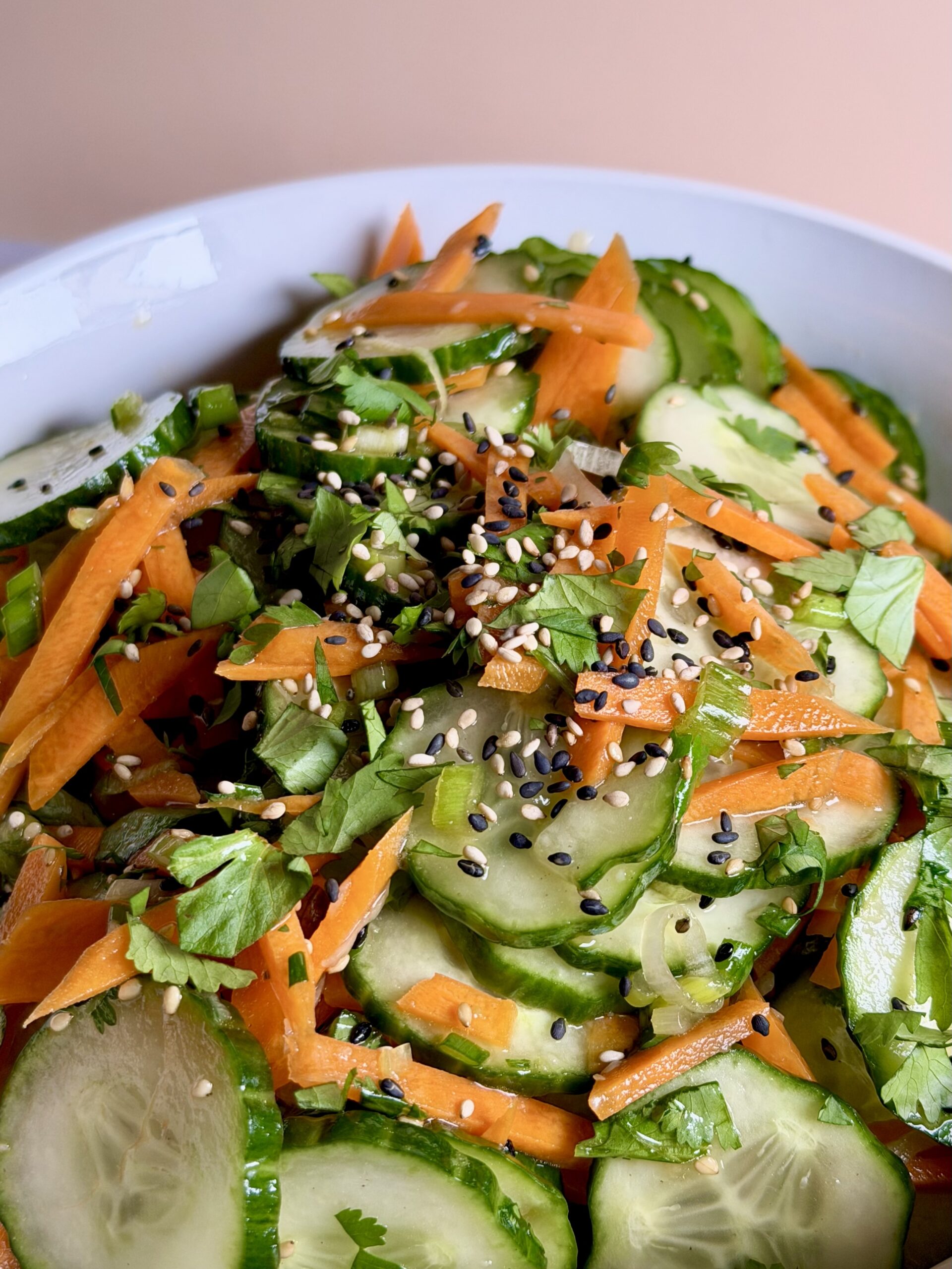 Close-up of Asian-style cucumber salad showing sliced cucumbers, carrots, herbs, and toasted sesame seeds
